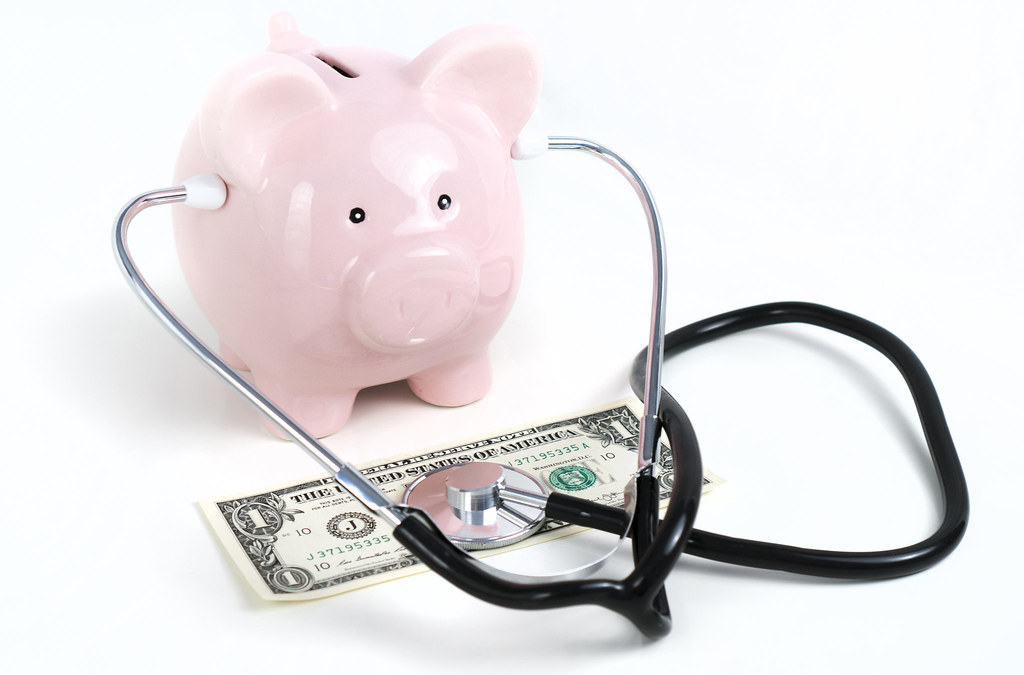 A piggy bank wearing a stethoscope and taking the pulse of a dollar bill