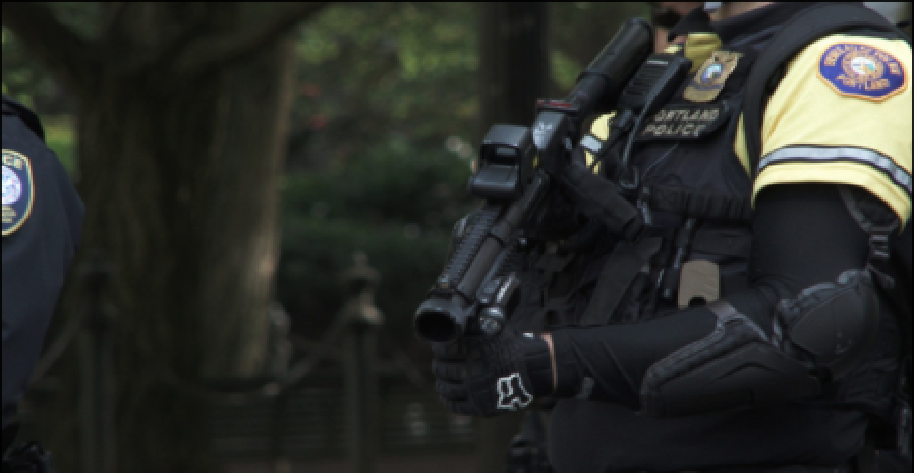 A portland oregon riot police officer holding a tactical style chemical grenade launcher in an "at rest" position.
